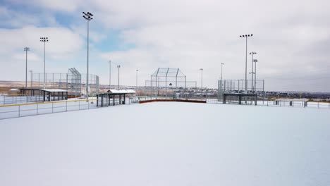 Baseball-and-softball-field-covered-in-fresh-powder-snow-during-the-day,-aerial-orbit