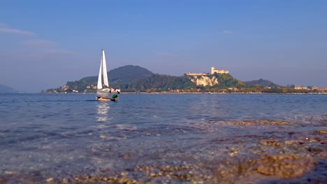 Low-angle-surface-view-of-lake-Maggiore-and-Angera-castle-with-boat-sailing-and-mallard-duck-swimming