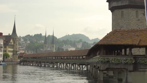 Historical-wooden-covered-Kapellbrucke-Bridge-and-Water-Tower-in-Reuss-River,-Church-of-St