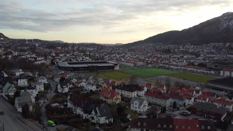 Goldener-Sonnenuntergang-Hinter-Dem-Brann-Fußballstadion-In-Der-Norwegischen-Stadt-Beren---Sich-Nach-Oben-Bewegende-Luftaufnahme