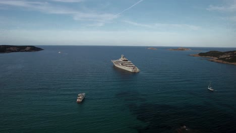 Aerial-wide-revealing-orbit-shot-over-the-Dilbar,-a-third-biggest-private-luxury-yacht-belongs-to-the-Russian-billionaire-Alisher-Usmanov-anchoring-on-the-emerald-waters-near-Porto-Cervo-in-Sardinia