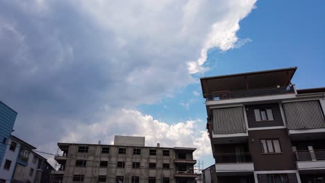 Low-angle-shot-in-timelapse-of-dark-rain-and-stormy-clouds-moving-in-blue-sky-over-residential-buildings-at-daytime