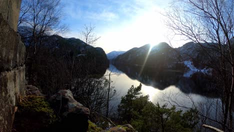 Weitwinkel-Sonnenuntergang-über-Dem-Veafjord-In-Norwegen-–-Wolken-Ziehen-Vorbei,-Während-Die-Sonne-Langsam-Hinter-Dem-Berg-Auf-Der-Insel-Osteroy-Untergeht-–-Spiegelungen-Im-Meer-Mit-Büschen-Und-Bäumen-Im-Vordergrund