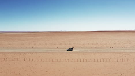 Vehículo-Automóvil-Blanco-Suv-Conduciendo-Por-Un-Camino-De-Grava-En-Un-Paisaje-Arenoso-En-Namibia---Disparo-De-Drones