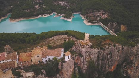 Aerial-drone-cinematic-4K-footage-of-a-battlement-and-a-village-on-top-of-a-rock-where-a-large-reservoir-of-turquoise-water-can-be-seen