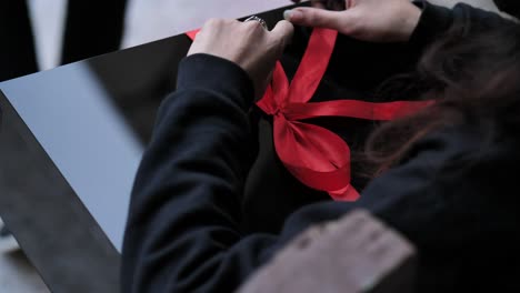 Over-Shoulder-View-Of-Female-Opening-Present-Tied-With-Red-Ribbon