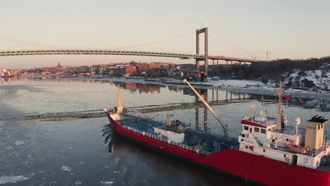 Drone-shot-over-a-big-red-fishing-boat-near-a-big-beautiful-bridge-in-Gothenburg,-Sweden