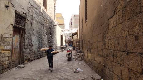 Authentic-real-life-scene-of-Egyptian-child-walking-in-old-street-of-Cairo-with-trays-of-bread-in-hands,-Egypt