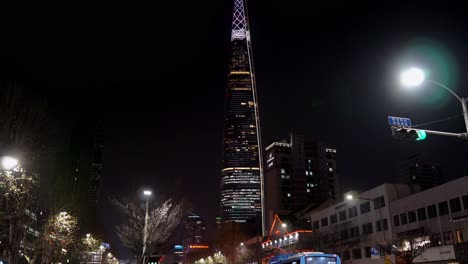 Tilt-up-on-Lotte-World-Tower-at-night-while-people-in-protective-masks-waiting-bus-at-bus-stop