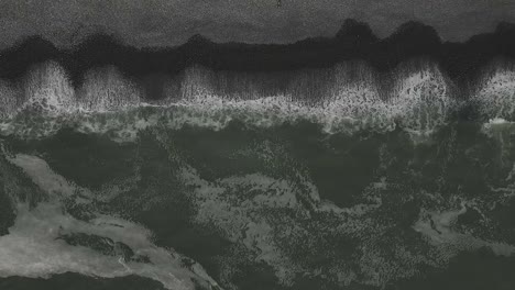 Am-Schwarzen-Kiesstrand-Bilden-Sich-Muster,-Während-Schmutzige-Meereswellen-An-Die-Küste-Spülen
