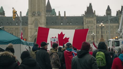 Freedom-Convoy-2022---Group-Of-Protestors-With-Canadian-Flag-In-Front-Of-Parliament-Building-In-Ottawa,-Ontario-Canada