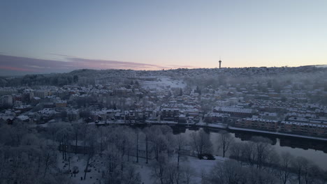 Aerial-View-Of-Trondheim-City-Covered-With-Fresh-Snow-With-Tyholt-Tower-In-The-Distance-At-Winter-In-Norway
