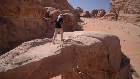 Mann-Geht-Auf-Einer-Natürlichen-Sandsteinbogenbrücke-Mit-Atemberaubendem-Aussichtspunkt-Auf-Die-Wüstenlandschaft-Von-Wadi-Rum,-Jordanien