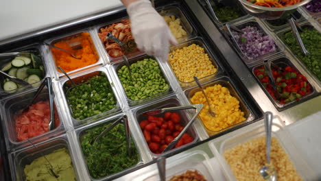 Worker-assembles-colorful-salad-at-vegetable-station-in-restaurant,-slow-motion-slider-4K