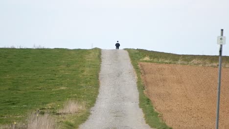 A-cyclist-pedalling-along-a-gravel-road-between-two-fields-on-a-cloudy-day
