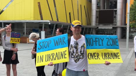 A-gentleman-holding-on-to-a-sign-stating-stop-war-in-Ukraine-and-no-fly-zone-over-the-airspace-in-Ukraine-at-the-peaceful-rally-held-at-downtown-Brisbane-square,-Queensland,-Australia