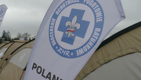 Flag-of-the-air-ambulance-service-waves-with-the-wind,-where-volunteers-help-with-rescues,-at-the-base-camp-for-refugees-at-the-Ukraine-Poland-border-crossing-in-Medyka,-Subcarpathian-province