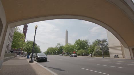 A-slow-motion-push-into-the-Washington-Monument-under-a-bridge-with-moving-taffic-in-Washington,-DC