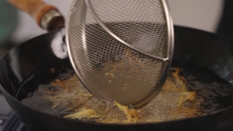 Slow-motion-close-up-shot-of-tasty-and-crispy-pai-potatoes-deep-frying-in-hot-oil,-professional-chef-using-strainer-to-mix-and-making-sure-all-surfaces-are-cooked-evenly