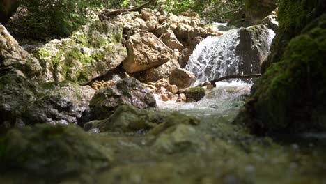 Low-Angle-Aufnahme-Eines-Kleinen-Wasserfalls,-Der-Bei-Sonnenlicht-Zwischen-Felsen-In-Den-Alpen-Fließt