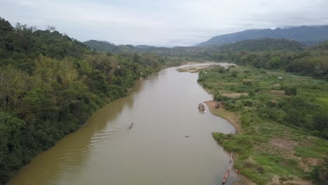 Aerial-descends-to-small-boat-navigating-river-in-dense-Laos-jungle