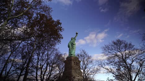 POV-walking-through-trees-towards-the-Statue-of-Liberty-in-New-York,-USA