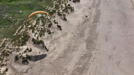 Paraglider-sailing-over-Dutch-beach-sand-dunes-casting-shadow