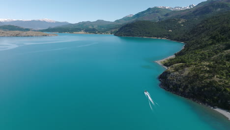 Aerial-Flying-Over-Smooth-Turquoise-Lake-General-Carrera-With-Speedboat-Travelling-Past-Coastline