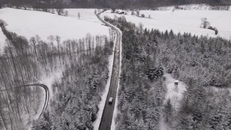 Two-cars-travelling-along-an-open-road-through-snow-covered-forest-and-fields-in-the-picturesque-countryside-of-West-Germany,-Europe