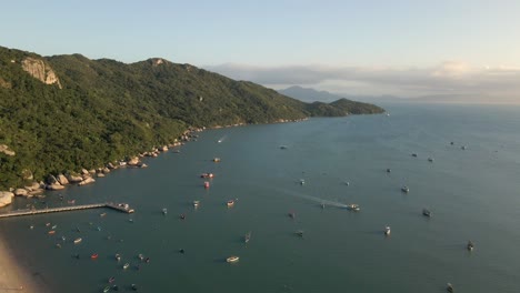 Small-Boats-Anchored-in-the-Sea-with-Green-Mountain-Coastline,-Aerial