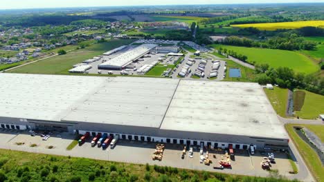 Buildings-of-logistics-center,-warehouses-near-the-highway,-truck-parking-process,-view-from-height,-a-large-number-of-trucks-in-the-parking-lot-near-warehouse