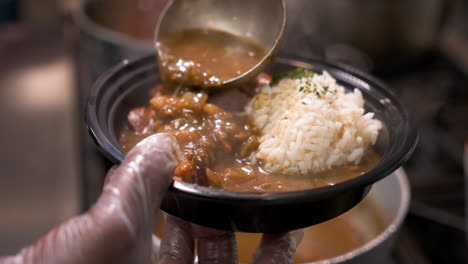 Cook-ladles-dark-rich-steaming-gumbo-into-bowl-over-white-rice,-slow-motion-close-up-4K