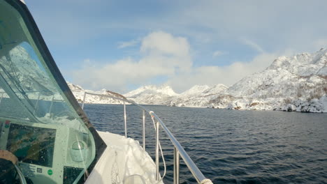 View-from-outside-the-cockpit-of-a-boat-as-it-cruises-around-Vesterålen-Norway-on-a-bright-sunny-day,-with-some-clouds-and-snow-capped-mountains