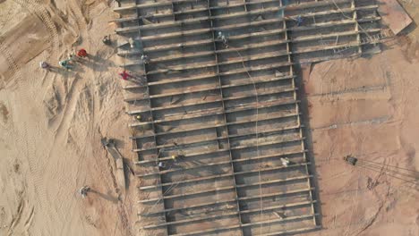 Aerial-Looking-Down-At-Steel-Lattice-Frame-On-Beach-At-Workers-Beside-It-At-Gadani-In-Pakistan