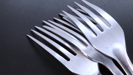 Detail-shot-of-four-steel-forks-face-down-on-a-black-bacground,-rotating-motion