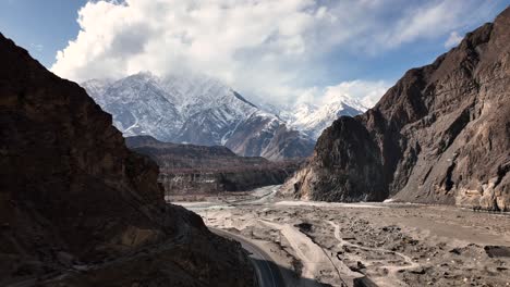 Drone-Flying-Through-Shadow-Of-Valley-To-Reveal-Snow-Capped-Mountains-Of-Hunza-Valley