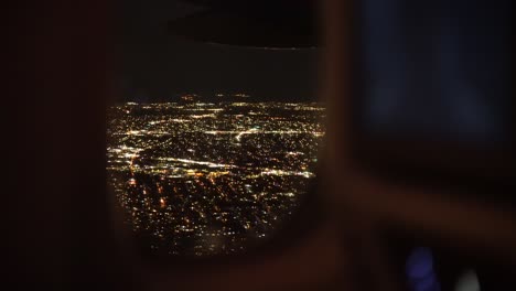 View-of-modern-cityscape-illuminated-at-night-from-airplane-window