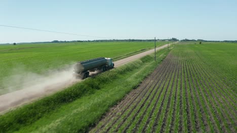 Aerial,-fuel-truck-driving-on-unpaved-countryside-farm-land-dirt-road