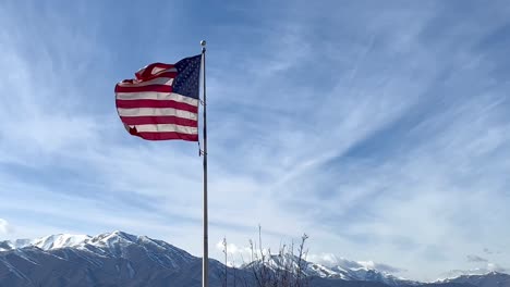 An-American-flag-waves-in-the-breeze-of-a-cloud-streaked-sky-with-a-scenic-mountain-range-in-the-background