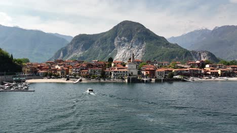 Low-Aerial-dolly-shot-of-beautiful-villa-on-the-end-of-a-lake-with-majestic-towering-mountains-and-a-boat-coming-into-dock-at-the-peaceful-beach