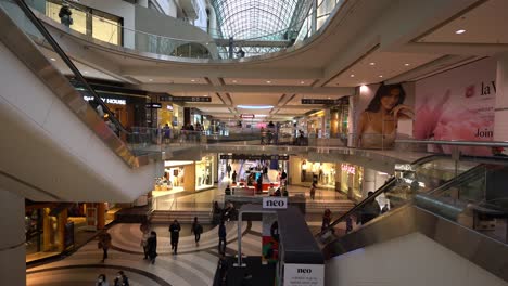 Natural-light-filters-through-a-glass-ceiling-illuminating-multiple-levels-of-large-shopping-mall,-the-CF-Toronto-Eaton-Centre---People-walk-though-plaza-searching-for-stores---Ontario,-Canada
