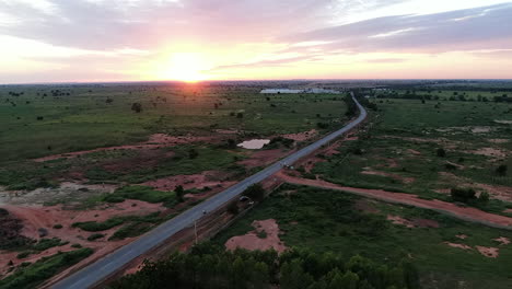 Ein-Leuchtend-Goldener-Sonnenuntergang-über-Der-Grünen-Und-Fruchtbaren-Landschaft-Nigerias-–-Luftaufnahme-Mit-Einem-Motorradfahrer,-Der-Eine-Einsame-Straße-Entlang-Fährt