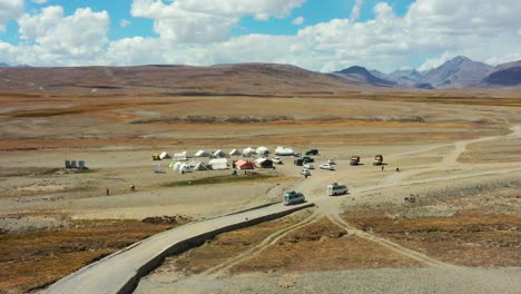 Aerial-drone-of-vans-carrying-cargo-and-tourists-arriving-at-a-campground-in-the-high-altitude-alpine-plain-of-Deosai-National-Park-located-between-Skardu-and-Astore-Valley-in-Pakistan-on-a-sunny-day