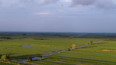 Dramatic-view-of-green-grass-fields-for-cattle-with-canals-for-irrigation-brightly-lit-with-dark-storm-clouds-in-the-background-for-beautiful-contrast---Netherlands,-aerial-orbiting-view
