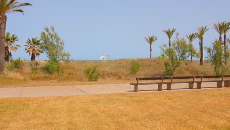 Empty-Wooden-Bench-In-The-Promenade-Overlooking-The-Blue-Sea-During-Summer