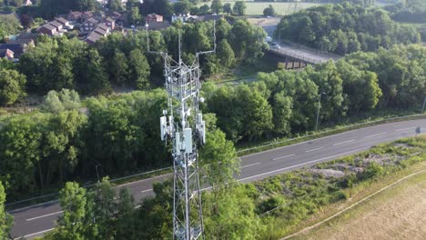5G-broadcasting-tower-antenna-in-British-countryside-with-vehicles-travelling-on-roads-background-aerial-tilting-down-view