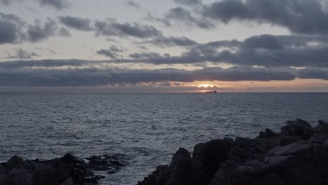 Cargo-ship-in-distant-ocean-horizon-during-sunset-golden-hour