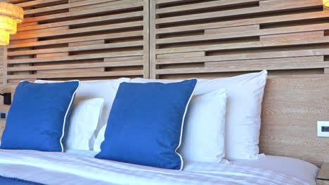 Hotel-Kingsize-gemachtes-Bett-Mit-Blauen-Und-Weißen-Kissen-Und-Eingeschalteten-Nachtlampen,-Handpfanne