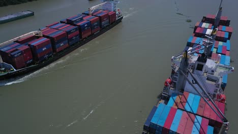 Aerial-panning-view-of-large-container-ships-passing-each-other-along-the-Saigon-river-in-Ho-Chi-Minh-City,-Vietnam-on-sunny-day-with-a-clear-blue-sky-and-low-air-pollution