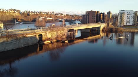 Bridge-between-Smieoya-and-Klosteroya-islands-in-Telemark-channel-skien-Norway---Cars-passing-bridge-during-sunset-hours-with-beautiful-reflections-in-water-surface